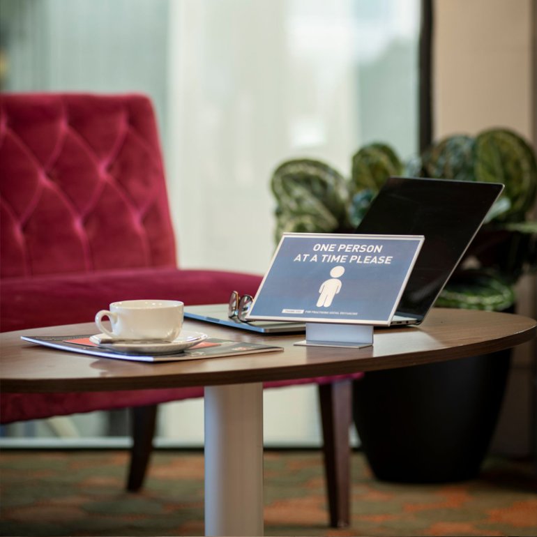 Absolute Freestanding Label holder placed on a table in an office environment informing social distancing measures. Absolute Freestanding Label holder placed on a table in an office environment informing social distancing measures.